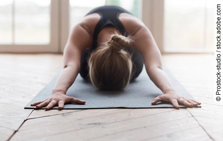 Blonde woman laying face down on yoga mat, stretching